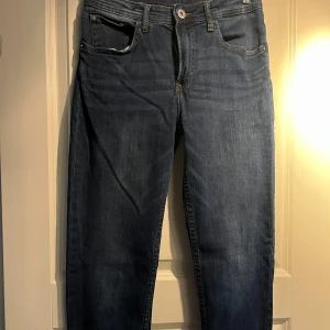 Blå jeans med relaxed tapered fit - Säljer ett par snygga blå jeans med relaxed tapered fit. De är i storlek 38 och har en bekväm passform. Perfekta för vardagsbruk och kan matchas med nästan vad som helst. De har en klassisk femficksdesign och är tillverkade i ett slitstarkt denimtyg.