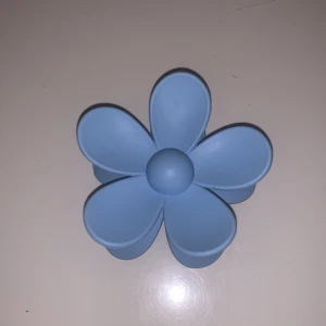 Blå blomformad hårklämma - Säljer en söt blå hårklämma i form av en blomma. Perfekt för att sätta upp håret på ett stilfullt sätt. Klämman är gjord av plast och har en stark fjäder som håller håret på plats. Passar både till vardags och festliga tillfällen.
