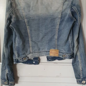 Blå jeansjacka från Place du Jour - Säljer en snygg blå jeansjacka från Place du Jour i storlek 34/XS. Jackan har en vintage-look med slitna detaljer och knappar framtill. Den har två bröstfickor med lock och knappar samt två sidofickor. Perfekt för vår och höst! 💙