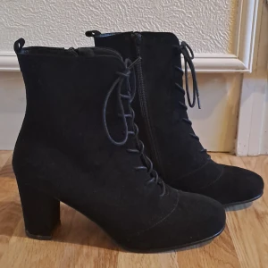 Svarta stövletter med snörning - Snygga svarta stövletter i mocka med snörning och dragkedja på sidan. De har en bekväm klack som ger lite extra höjd utan att kompromissa med komforten. Perfekta för höst och vinter, och funkar lika bra till vardags som till fest.