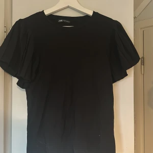 Svart topp från Zara - Säljer en stilren svart topp från Zara. Den har korta puffärmar som ger en fin volym.