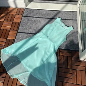 Mintgrön ärmlös klänning - Säljer en superfin mintgrön klänning i ett lätt och luftigt material. Den är ärmlös och har en elegant, flödande design som passar perfekt för sommarens alla fester. Klänningen har en hög halsringning och en vacker, asymmetrisk fåll som ger en extra touch av stil.