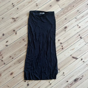 Svart långkjol - Säljer en elegant svartgrå långkjol i ett mjukt och stretchigt material. Perfekt för både vardag och festliga tillfällen. Kjolen har en enkel och stilren design som gör den lätt att matcha med olika toppar och accessoarer.