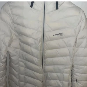 Vit pufferjacka från Everest - Säljer en snygg vit pufferjacka från Everest. Den är perfekt för kalla dagar med sin quiltade design och dragkedja framtill. Jackan har en stilren look och är supervarm. Perfekt för vintern! ❄️