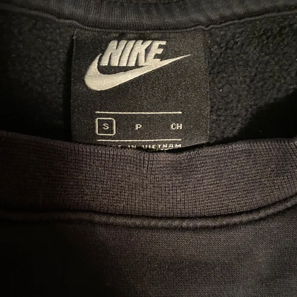 Säljer en svart sweatshirt från Nike i storlek S. Tröjan har en stor vit Nike-logga och röd text på baksidan som ger en sportig look och dubbel logga där fram. Materialet känns mjukt och bekvämt. Passar perfekt för hösten! . Tröjor & Koftor.