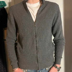 Massimo dutti zip up - Säljer en stilren grå stickad kofta med dragkedja framtill. Den har en diskret textur och ribbade muddar vid ärmslut och nederkant. Perfekt för både vardag och lite finare tillfällen. Strl M