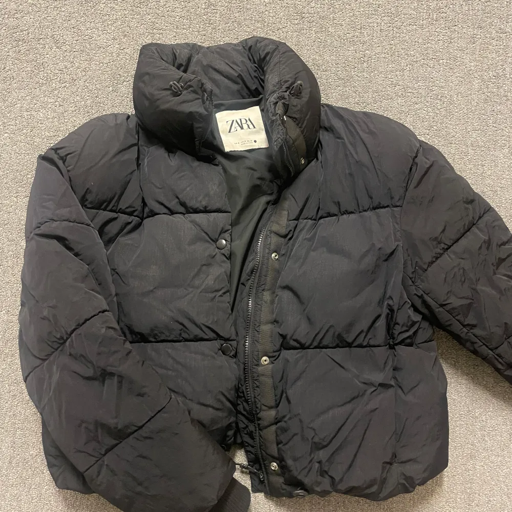 Snygg svart pufferjacka från Zara med hög krage och dragkedja. Perfekt för kyliga dagar med sin vadderade design. Fin passform som ger en modern look.. Takit.
