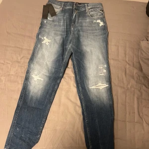 Blå jeans från Replay - Säljer ett par snygga blå jeans från Replay i sprillans nytt skick. Storlek 30 30. De har en cool slitningseffekt på framsidan och en klassisk femficksdesign. Perfekta för både vardag och fest! 🕺sitter lite mer pösigt än de vanliga slim fit byxorna. Nypris 1500. Mitt pris 849
