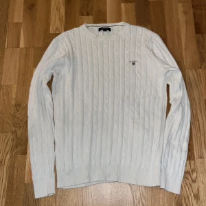 Vit kabelstickad tröja från Gant - Säljer en stilren vit kabelstickad tröja från Gant. Den har en klassisk design med ribbade muddar och rund hals. Perfekt för både höst och vinter, och funkar lika bra till vardags som till lite finare tillfällen. Tröjan är i mycket bra skick och redo för en ny ägare!