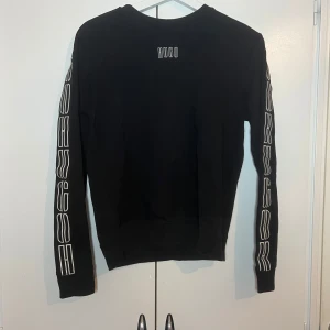 Svart långärmad tröja från Hugo o byxa - Snygg svart långärmad tröja från Hugo med vit logga på bröstet och längs ärmarna. Perfekt för en stilren look. Har även en matchande byxa. På byxan har plasten går av ena sidan. Men det går att byta ut