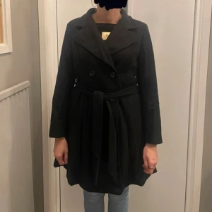Svart kappa - Säljer en stilren svart kappa från Shein i storlek M. Har ett bälte i midjan för en snygg passform. Perfekt för höst och vår med sina långa ärmar och klassiska design. Kappan är i mycket bra skick och redo för nya äventyr!