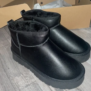 Svarta uggs - Säljer ett helt nytt par svarta uggs i syntetmaterial med mjukt foder inuti, gjorda av riktigt skinn. Perfekta för kalla dagar med sin varma insida. De har en enkel design utan snörning eller dragkedja, vilket gör dem lätta att ta på och av. Passar bra till både vardag och mer avslappnade tillfällen. Dem är från polen💕