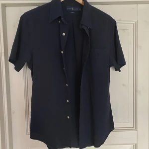 Kortärmad skjorta från Ralph Lauren - Säljer en stilren mörkblå kortärmad skjorta från Ralph Lauren. Riktigt skönt material så perfekt t sommaren eller tillfällen där du vill vara lite uppklädd!🍻helt ny!