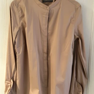 Beige skjorta från Mos Mosh - Säljer en stilren beige skjorta från Mos Mosh i storlek L. Skjortan har en enkel design med långa ärmar. Perfekt för både vardag och festliga tillfällen. Materialet känns mjukt och bekvämt mot huden.