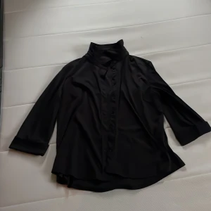 Svart skjorta från Hennes Collection - Säljer en elegant svart skjorta från Hennes Collection i storlek 50/52. Skjortan har långa ärmar och knappar framtill. Perfekt för både vardag och festliga tillfällen. Materialet känns mjukt och bekvämt mot huden. Är dessutom utav stretchigt material. Passar utmärkt till höst- och vintergarderoben. 🖤
