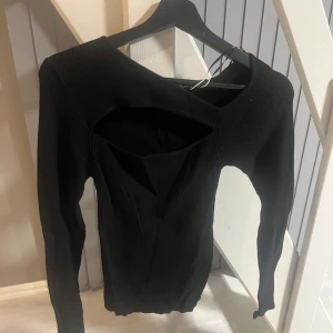 Svart ribbad topp med cutout - Snygg svart ribbad topp från Gina tricot med en unik cutout-design framtill. Perfekt för att ge din outfit en trendig touch. Toppen har långa ärmar och en tight passform. Den är i storleken M skulle säker också pappa som S. Har aldrig använt så som ny. 