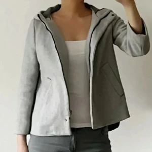 Trekvartsärmad kappa med huva - BARA SERIÖSA KÖPARE PLS! Säljer en stilren och mysig grå kappa/jacka med huva. Perfekt för höst. Använd ett fåtal gånger så i bra skick. Storlek M. Använd gärna KÖP NU om du vill köpa.