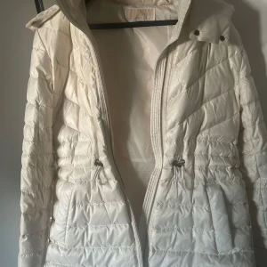 Micheal kors jacka - Säljer en snygg vit quiltad dunjacka med huva. Jackan har dragkedja och justerbar midja för perfekt passform. Perfekt för kyliga höst- och vinterdagar. Den är i mycket bra skick och redo för nya äventyr!