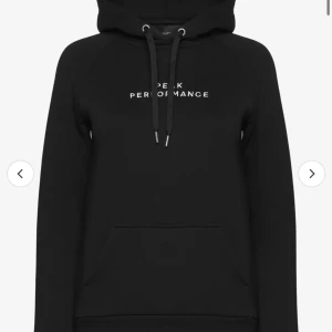 Svart hoodie från Peak Performance - Snygg svart hoodie från Peak Performance med vit text på bröstet. Den har en klassisk känguruficka och justerbar dragsko i huvan. Perfekt för en avslappnad stil.