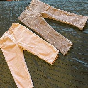 Två par barnbyxor i olika stilar - Säljer två par barnbyxor. Ett par är rosa manchesterbyxor med elastisk midja och bakfickor. Det andra paret är grå byxor med vita prickar och klassisk femficksdesign.