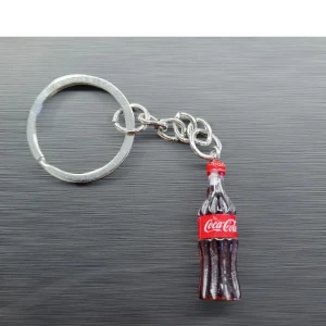 Nyckelring med Coca-Cola-flaska - Cool nyckelring med en liten Coca-Cola-flaska som hänge. Flaskan är detaljerad med den klassiska röda etiketten och ser nästan ut som en riktig miniatyr. Perfekt för att piffa upp dina nycklar eller som en rolig present till en Coca-Cola-älskare!