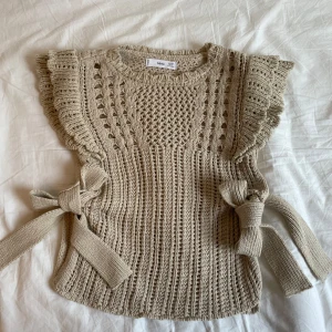 Beige stickad topp från MNG - Säljer en superfin beige stickad topp från MNG. Den har ett unikt mönster med volangdetaljer på axlarna och knytband på sidorna så det är som en väst🥰
