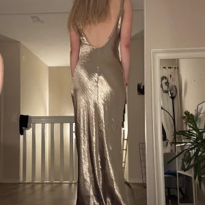 Guldfärgad långklänning med öppen rygg - Säljer en elegant guldfärgad långklänning i syntetmaterial. Klänningen har en öppen rygg och smala axelband. Perfekt nu till balen eller liknande.  Säljer för att jag har hittat en annan balklänning, men älskar denna! Är 173cm och klänningen går ner till fötterna💕