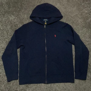 Mörkblå hoodie från Polo Ralph Lauren - Säljer en snygg mörkblå hoodie från Polo Ralph Lauren i storlek XL (barnstorlek) eller XS/S vuxen storlek. Den har en dragkedja framtill och det klassiska röda Polo-logotypen broderad på bröstet. Perfekt för höst och vinter, och den är i mycket bra skick. Passar både till vardags och lite mer avslappnade tillfällen. (Accepterar endast Swish pga lurendrejerier) (Checka även in andra kläder på min profil och köp tillsammans för ett rabatterat pris) 