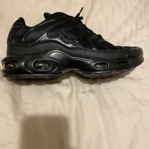 Svarta sneakers från Nike - Snygga svarta sneakers från Nike med en futuristisk design och synliga luftkuddar i sulan. Skorna har snörning och en robust konstruktion som ger bra stöd och komfort. Perfekta för en sportig look.