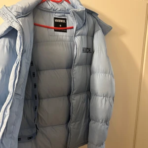 Ljusblå pufferjacka från Hoodrich - Snygg ljusblå pufferjacka från Hoodrich med broderad logga på bröstet och ryggen. Jackan har en avtagbar huva och dragkedja framtill. Perfekt för kyliga dagar. Den är ett halvår gammal och ny pris på den är 2000kr köpt från hoodrich pris kan diskuteras 