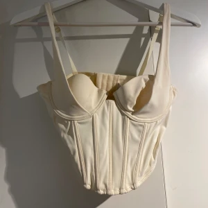 Korsett - Croppad korsett cremefärgad från NAKD. Storlek 75B i bysten men justerbart spänne baktill. 