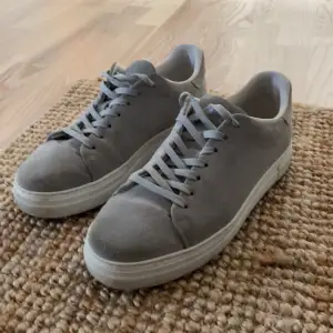 Säljer ett par stilrena grå sneakers i mocka. De har en klassisk design med snörning och en bekväm passform. Perfekta för vardagsbruk och passar till det mesta i garderoben. Litet hål i insidan av skon på hälen. Men inget som märks eller syns. Nypris 1299. Mitt pris 599. 