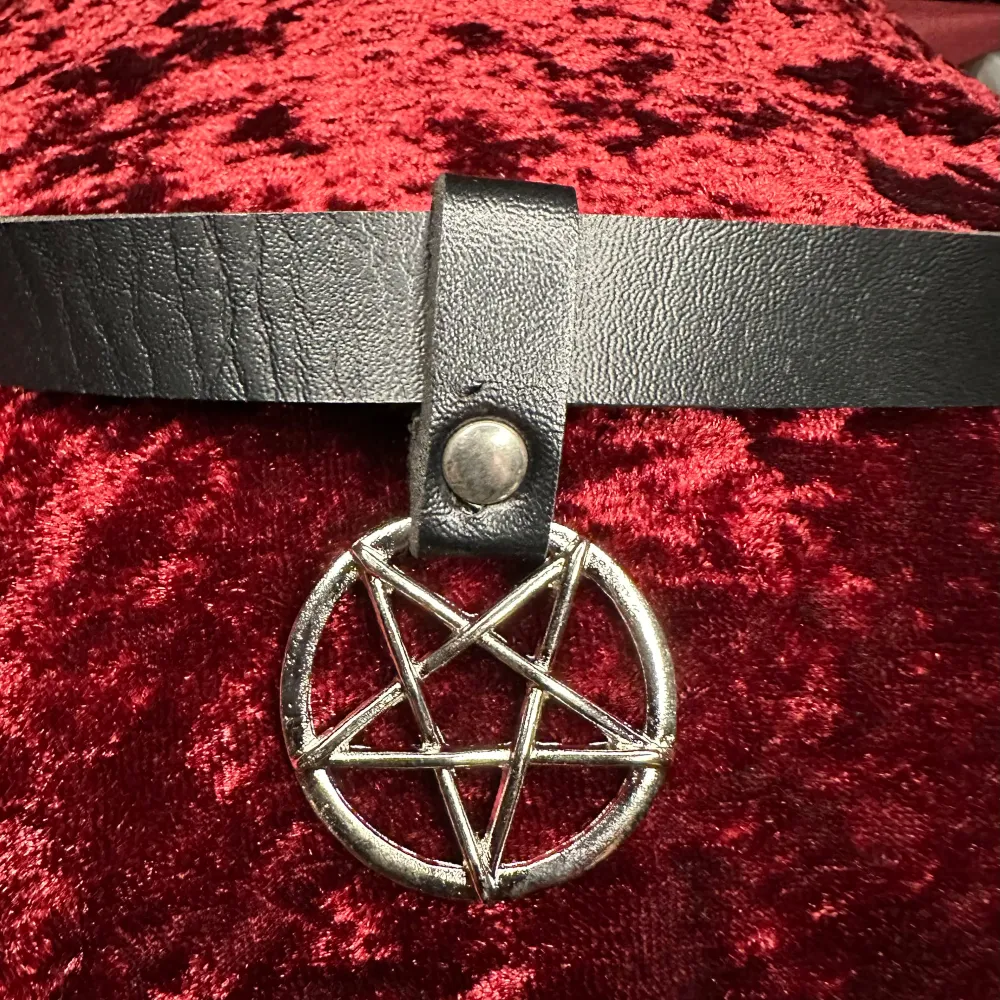 Fet choker med silverfärgat pentagram. Svart band i faux leather 2 cm brett, 43 cm långt. Pentagram 4,5 cm långt. Knäpps med tryckknappar, kan fästas i längd mellan 38 och 41,5.  Unisex.  Ovanligt, ett riktigt statementsmycke. Nytt och oanvänt. . Accessoarer.