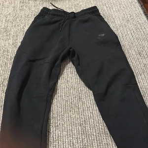 Svarta mjukisbyxor från Nike - Säljer ett par svarta mjukisbyxor från Nike. De är superbekväma och perfekta för chill dagar eller träning. Byxorna har en elastisk midja med snörning för bästa passform. De är i bra skick och redo för nya äventyr!