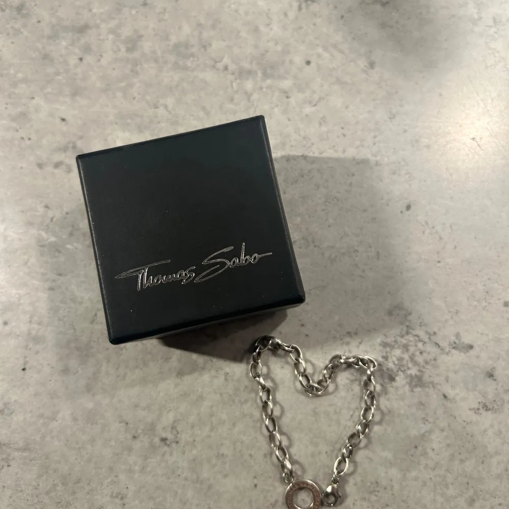 Säljer ett snyggt silverarmband från Thomas Sabo. Armbandet har en klassisk kedjedesign med en rund berlock där märkesnamnet är ingraverat. Perfekt för både vardag och fest!. Accessoarer.