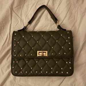 Mörkgrön handväska - En vadderad handväska med guldnitar i mörkgrön/mossgrön färg💕 Låset på väska har rostat lite men inget som man tänker på om man inte kollar nära (kolla tredje bild)!💝