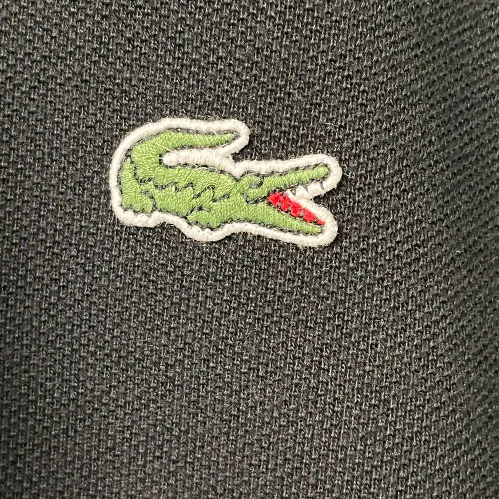 Säljer en klassisk svart pikétröja från Lacoste. Den har korta ärmar och en broderad Lacoste-logga på bröstet. Tröjan är i bomull och har en normal passform med knappar vid kragen. Perfekt för både vardag och fest!. T-shirts.