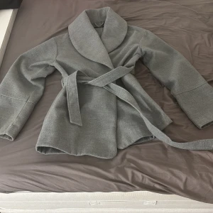 En grå kappa - Det är en grå kappa som värmer väldigt mycket, storlek S men den är väldigt stor så om du har storlek M på jackor passar denna kappan ändå dig. Den är kort men täcker rumpan. Knappt använd!