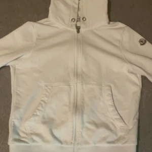 Vit huvtröja med dragkedja - Säljer en vit huvtröja med dragkedja. Den har en mysig och bekväm passform med långa ärmar och en praktisk ficka framtill. Huvan har snörning för justering. Pris kan diskuteras!!!