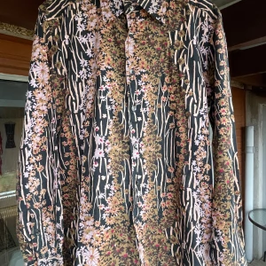 Blommig skjorta från Dolce & Gabbana - Säljer en supercool blommig skjorta från Dolce & Gabbana. Den har ett unikt mönster med blommor i rosa, beige och brunt på en svart bakgrund. Skjortan är långärmad och har knappar hela vägen ner. Perfekt för att sticka ut på festen eller bara för att känna sig extra stilren.