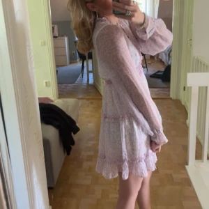 Ljusrosa blommig klänning - Säljer en superfin ljusrosa klänning med blommigt mönster. Den har långa ärmar och volangdetaljer vid ärmslut och nederkant. Perfekt för sommarens alla fester och midsommarfirande! 💖