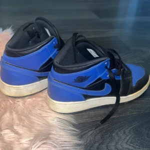 Blå och svarta Nike Air Jordans - Säljer ett par coola Nike Air Jordans i blått och svart. De har en klassisk design med snörning och en hög ankel. Skorna är lite använda men fortfarande i bra skick. Perfekta för både vardag och fest!