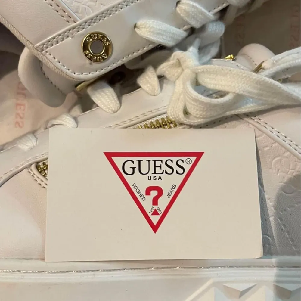Säljer ett par snygga vita sneakers från Guess. De har coola gulddetaljer som dragkedjor och logotyp på sidan. Skorna har en unik sula med mönster och är perfekta för att ge din outfit en lyxig touch. De är i nyskick och redo att bäras till både vardag och fest!. Kengät.