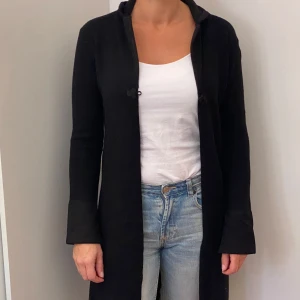 Svart kappa från KappAhl - Säljer en stilren svart kappa från KappAhl i storlek 34/36. Den har långa ärmar och knäpps med dekorativa knappar framtill. Perfekt för höst och vår, och funkar både till vardags och fest. 🖤