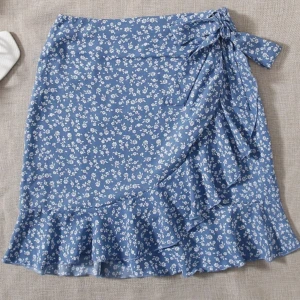 Blå knytkjol - Säljer denna fina blå kjolen med snören eftersom den inte har kommit till någon användning. Kjolen är luftig och flyger inte upp när det blåser vilket är underlättande för blåsiga sommardagar! Den har även en dragkedja vid sidan!