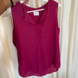 Lila ärmlös topp från Vila - Säljer en snygg lila ärmlös topp från Vila. Perfekt för sommardagar eller en kväll ute. Toppen har en enkel och stilren design med en lätt v-ringad hals. Materialet känns luftigt och bekvämt. Passar bra till både jeans och kjol!