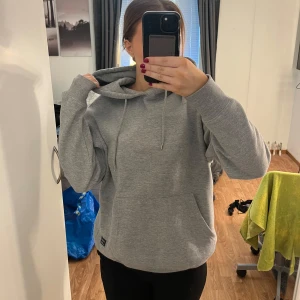 Grå hoodie i mycket bra skick - Säljer en supermysig grå hoodie i mycket bra skick. Den har en klassisk design med en stor ficka fram och justerbar huva. Perfekt för kyliga dagar eller bara för att chilla hemma. Passar till allt och är ett måste i garderoben! 
