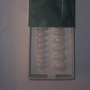 Glittriga vita lösnaglar - Säljer ett set med glittriga vita lösnaglar. Perfekta för att ge dina händer en extra touch av glamour. De kommer i olika storlekar för att passa alla naglar. Perfekt för fest eller speciella tillfällen!