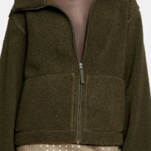 Olivgrön teddyjacka med dragkedja - Mysig olivgrön teddyjacka i syntetmaterial med dragkedja framtill. Perfekt för höst och vår, med en avslappnad passform och långa ärmar. Jackan är superbekväm och håller dig varm under kyliga dagar. Ett måste för garderoben!