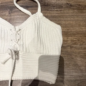Vit stickad topp med snörning - Säljer en superfin vit stickad topp med snörning framtill. Den är ärmlös och har en croppad passform, perfekt för sommardagar. 